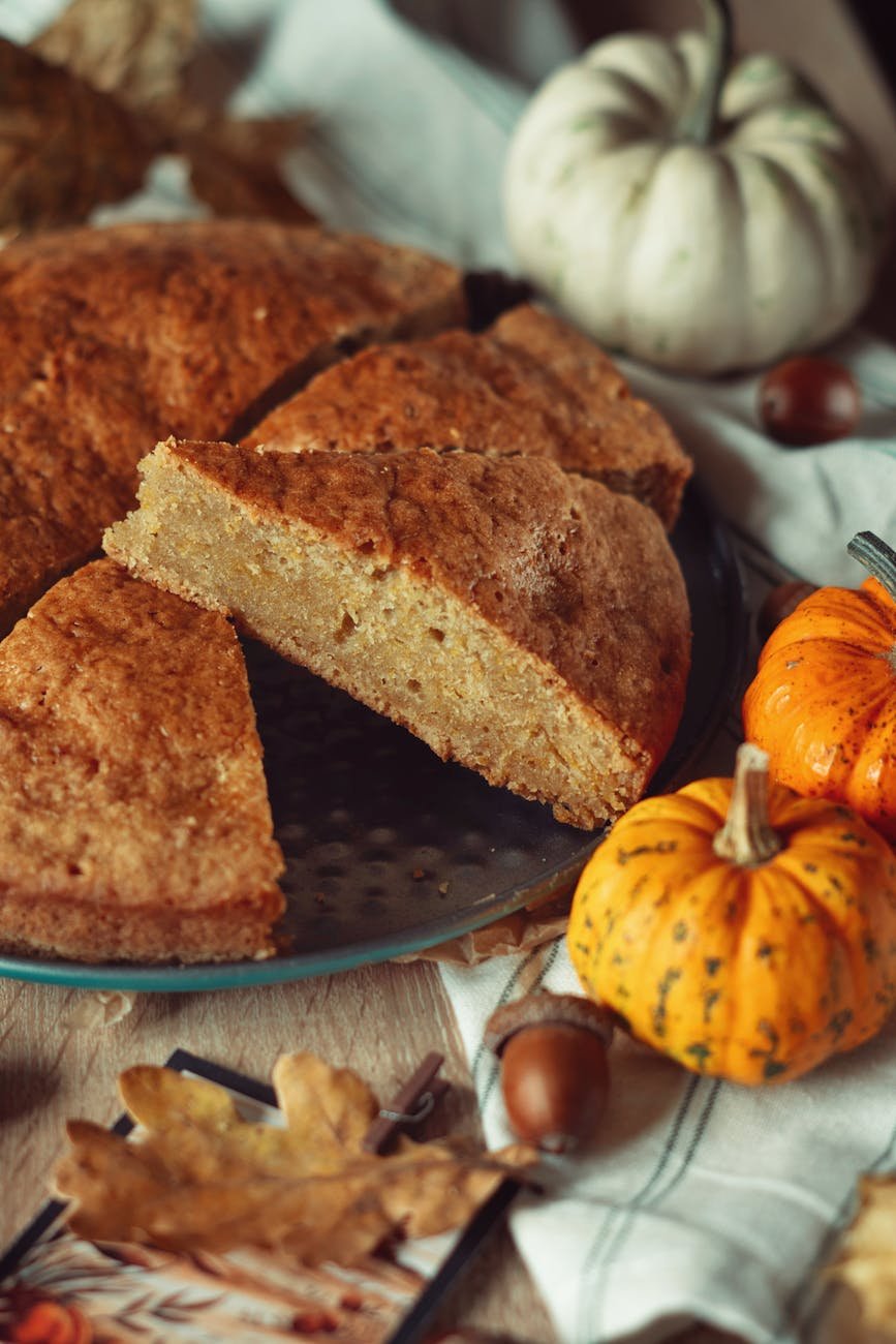 close up of a pumpkin cake on a baking tray with autumnal decorations lying around