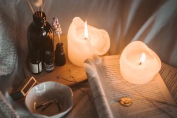 lighted candle on white book beside black glass bottle